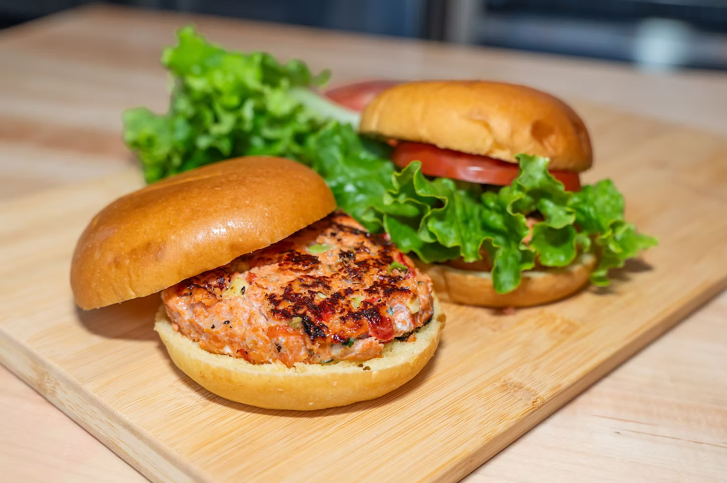 Wild Alaskan sockeye salmon burgers on a cutting board with lettuce and tomato