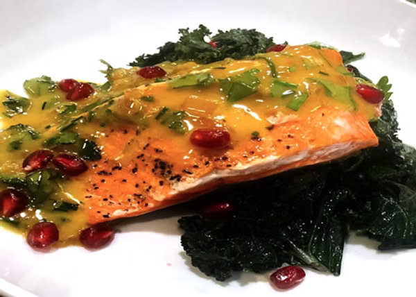 This dish features pan-seared Copper River Sockeye salmon topped with a rich Lilikoi (passion fruit) beurre blanc sauce. It’s topped with cilantro and pomegranate arils, all plated on a white plate.