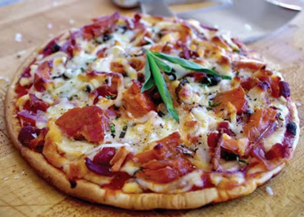This image shows a personal size pizza topped with marinara, cheese, smoked salmon, and bacon.