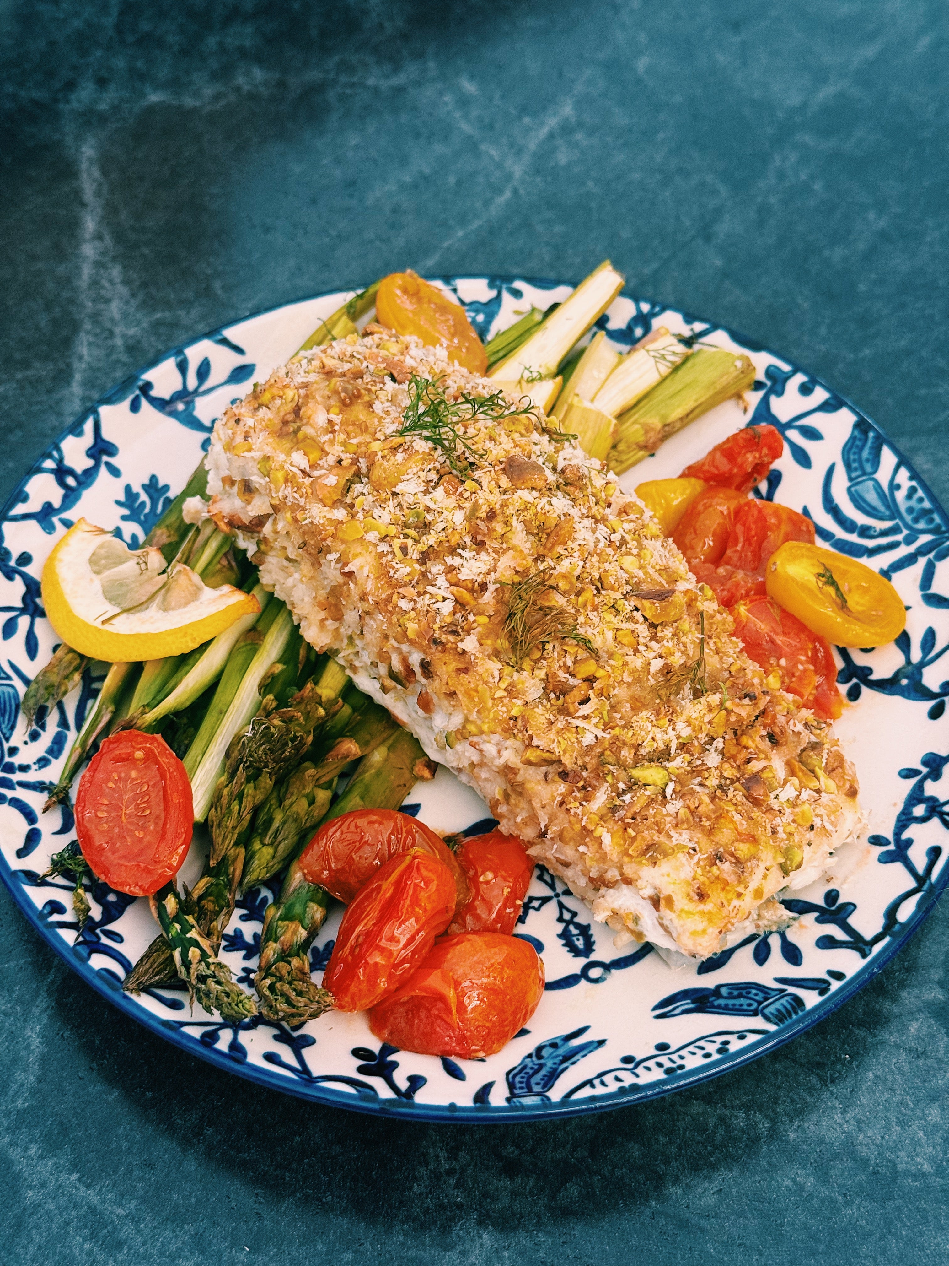Plated dish with roasted halibut, asparagus, and cherry tomatoes on a blue and white patterned plate.