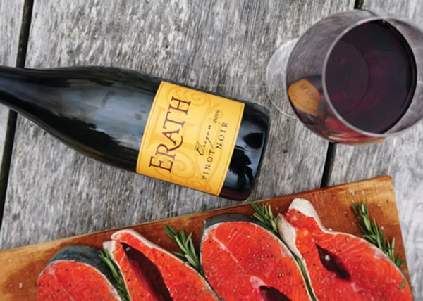 Salmon on a cutting board sitting next to a bottle and glass of red wine.