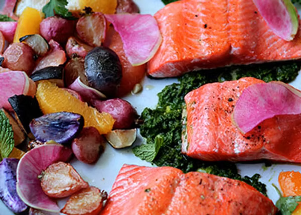 Copper River salmon on a platter accompanied by radishes, herb sauce, grapefruit, and oranges.