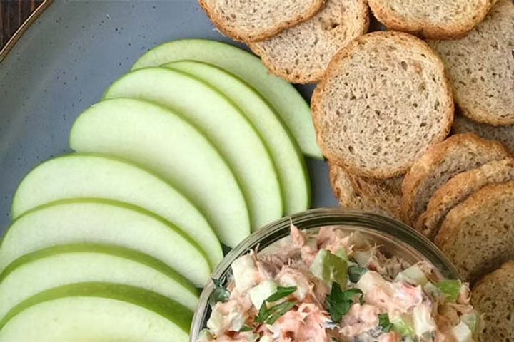 This image shows a bowl of smoked salmon apple dip next to sliced apples and toasts.