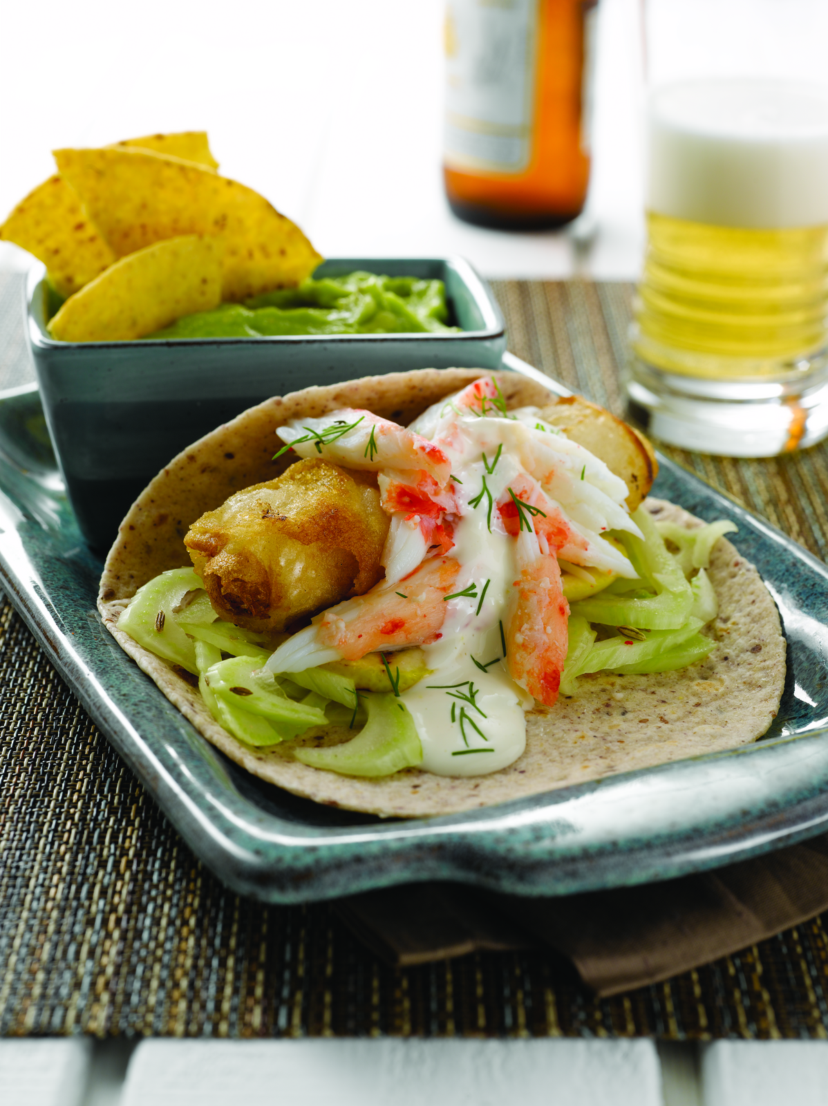 Tortilla with minced halibut and vegetables on a tray with a side of guacamole and chips