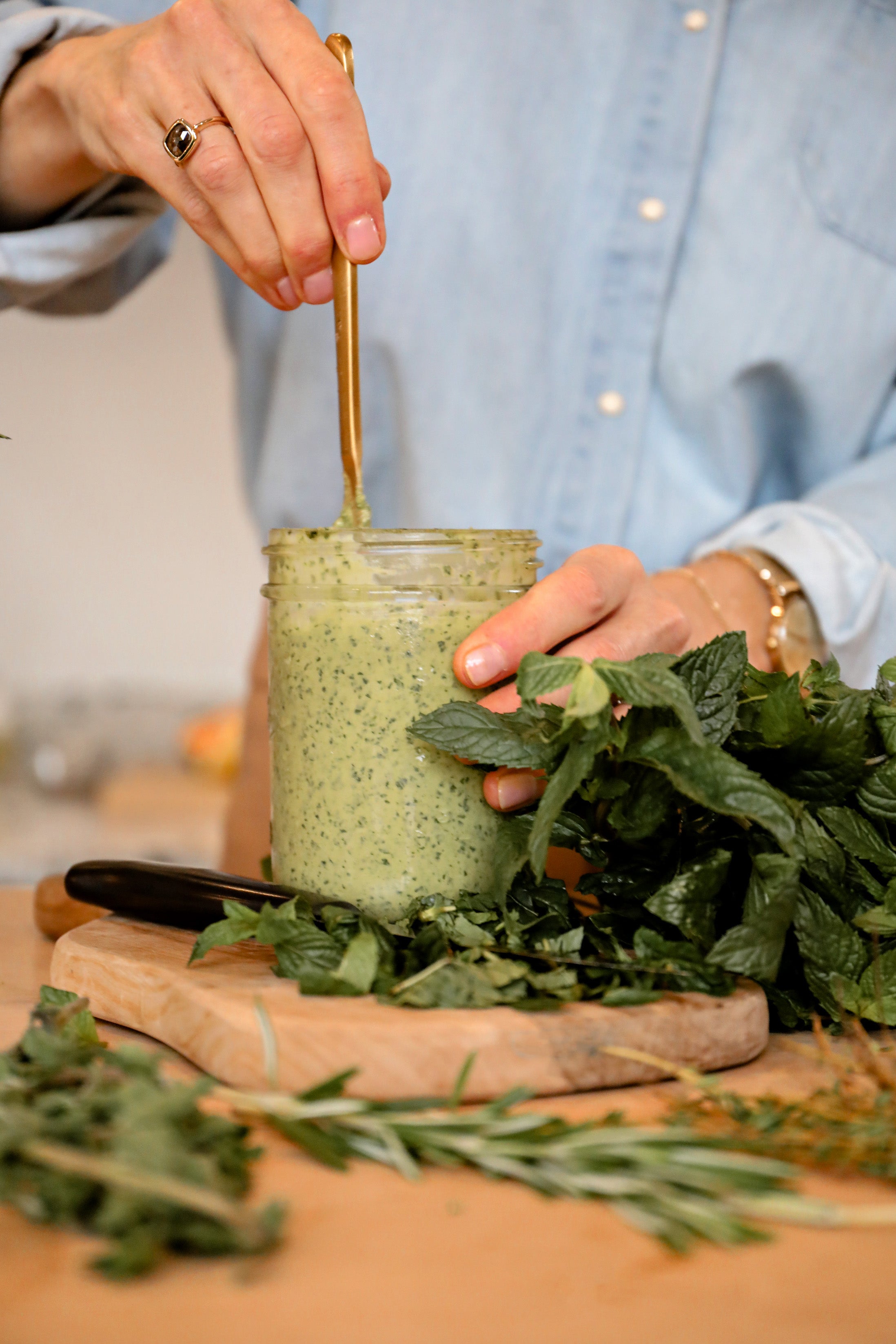 Person holding a jar of green goddess dressing with fresh herbs on a wooden surface
