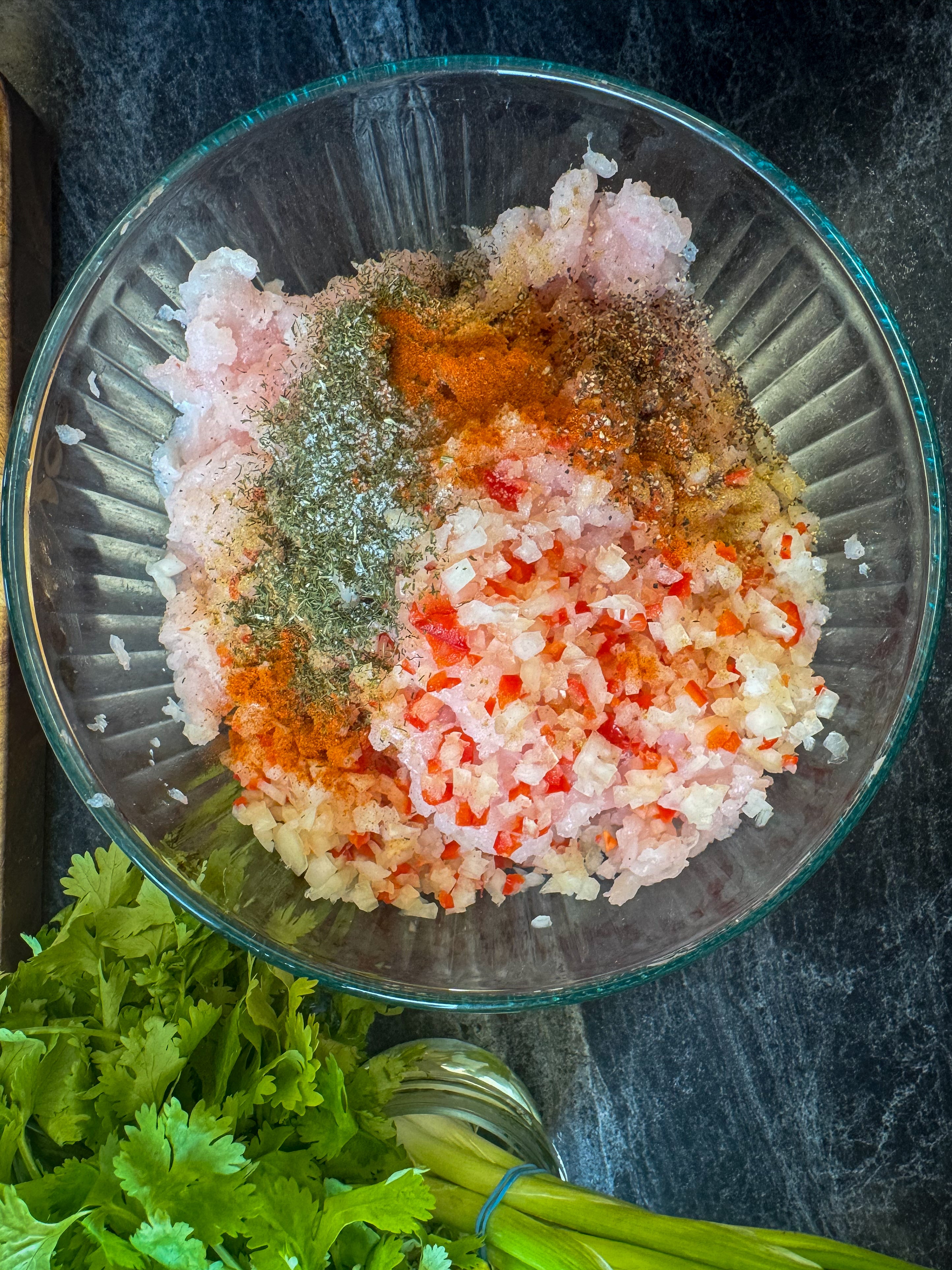 Glass bowl with minced halibut meat and spices with cilantro on the side