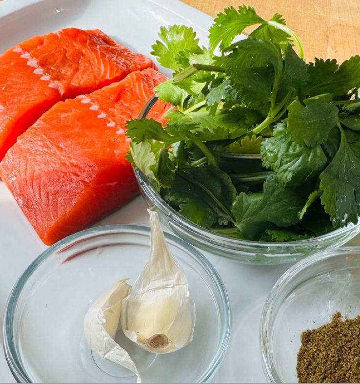 Raw salmon with cilantro, garlic, and spices on a white surface