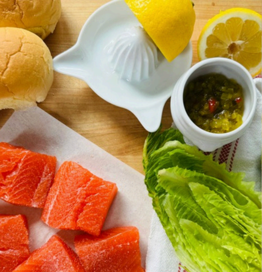Salmon slices, lemon, and condiment on a wooden board