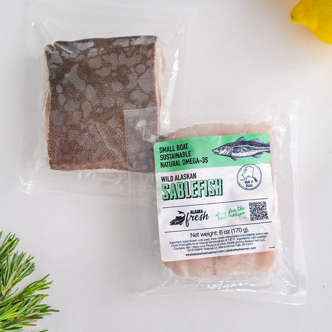 Packaged sablefish with a label on a white surface with rosemary and a lemon.