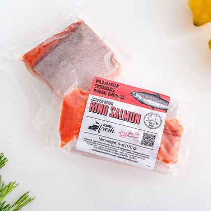 Packaged King Salmon with a label on a white surface with lemons and rosemary.