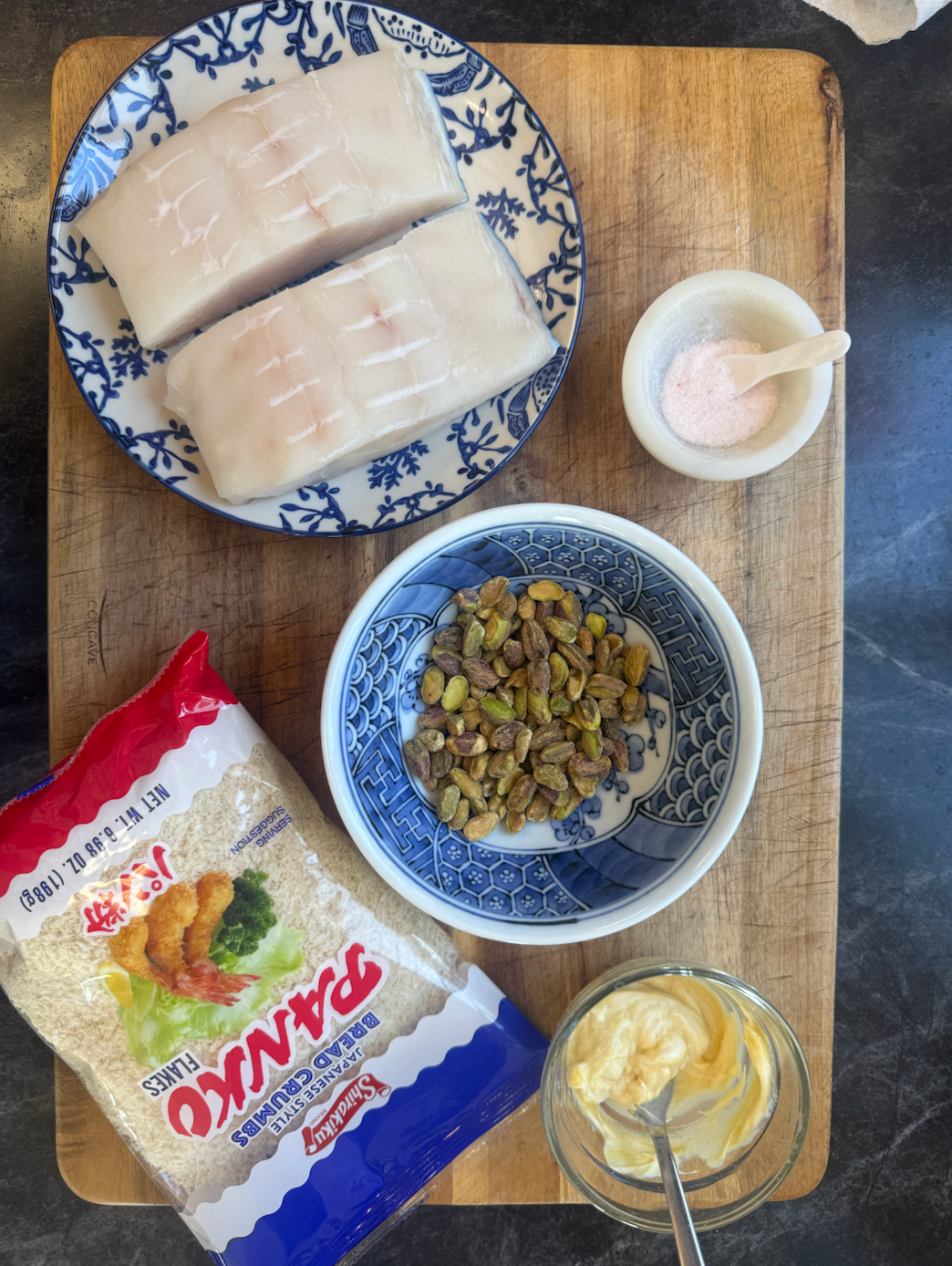  ingredients on a wooden board including panko breadcrumbs, a bowl of dried fruits, and a small container of mayonnaise.